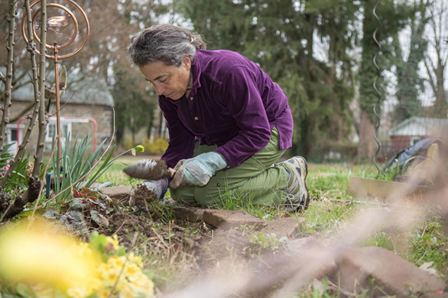 A person kneeling down and gardening with a trowel