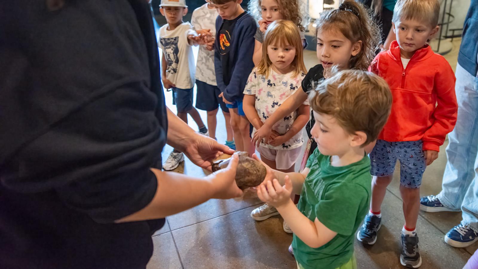 An academy educator showing off a fossil to a group of children.