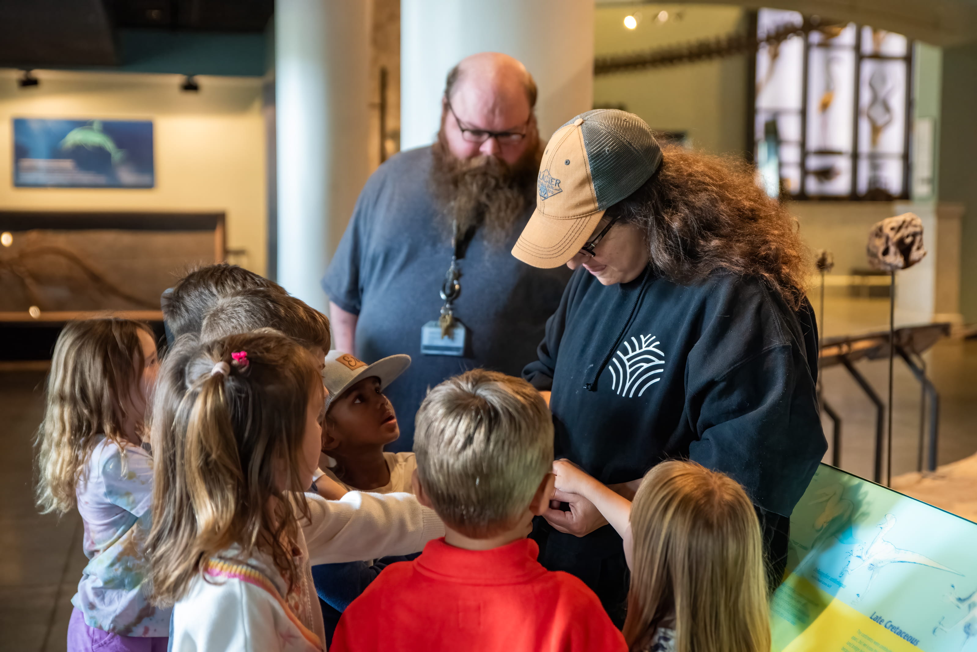 A group of school children looking at a fossil being shown to them by two educators.