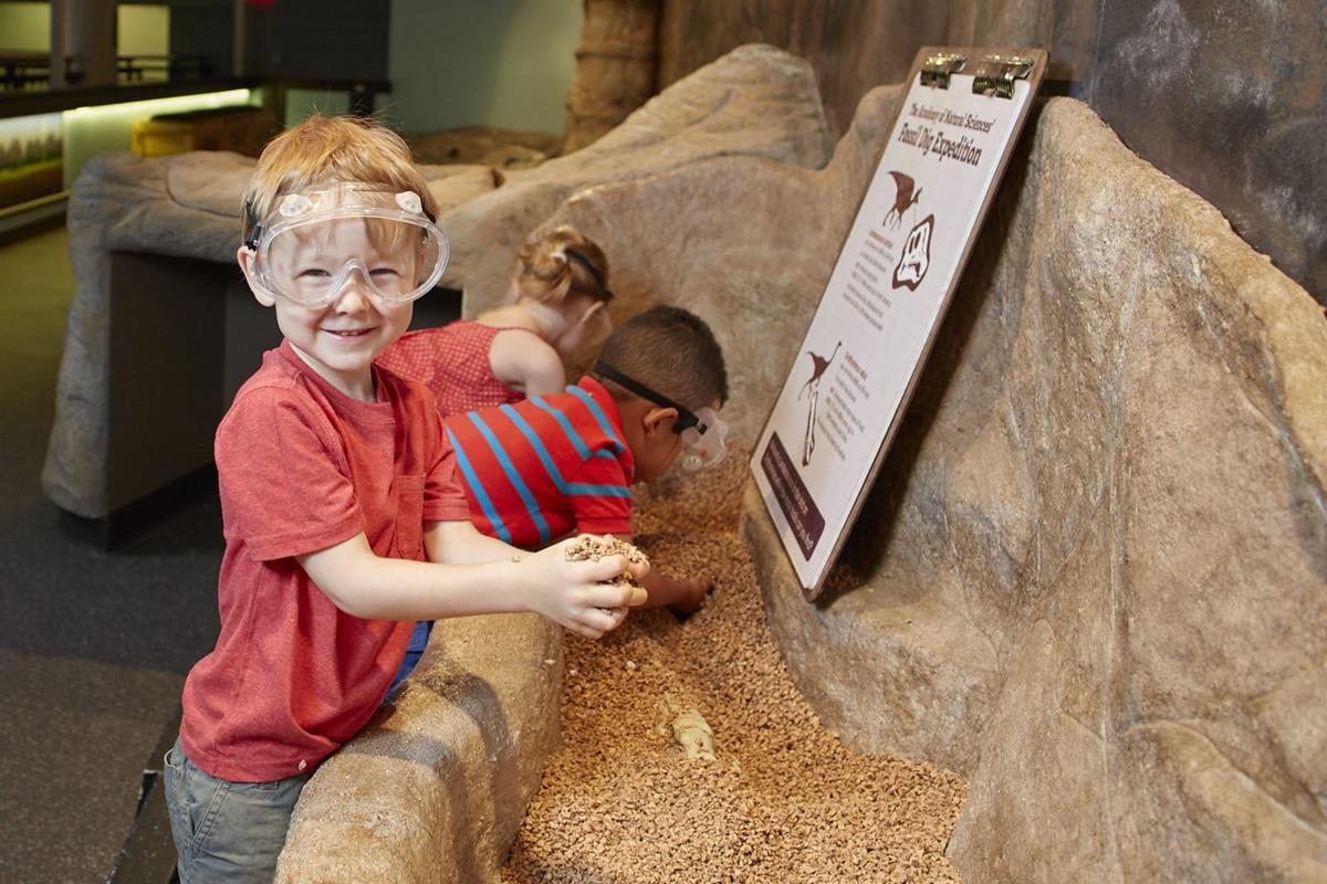 Three children looking for fossils in the big dig, all wearing goggles.