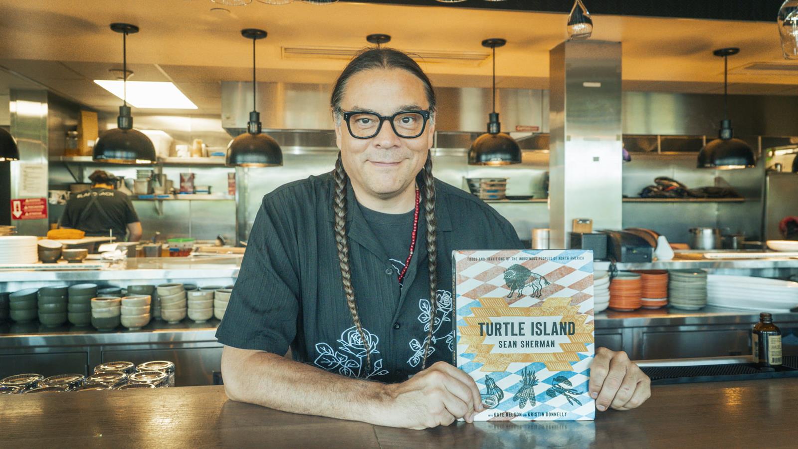 Sean Sherman holding their book in a resturant.