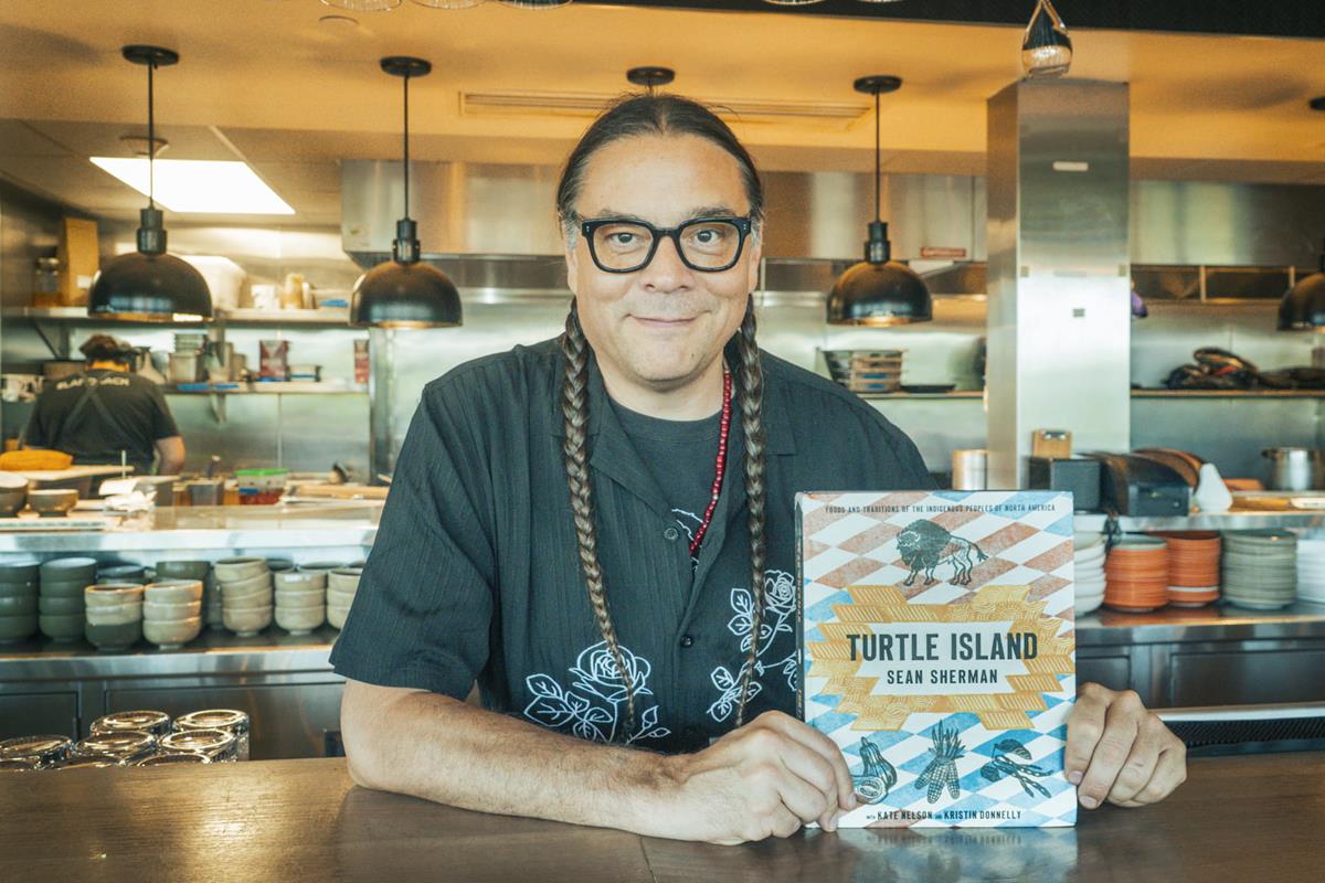 Sean Sherman holding their book in a resturant.