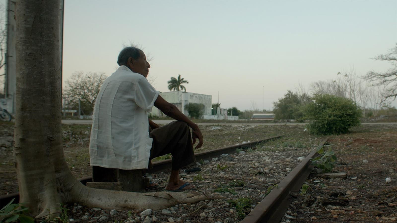 An image of an older man sitting on a railroad track.