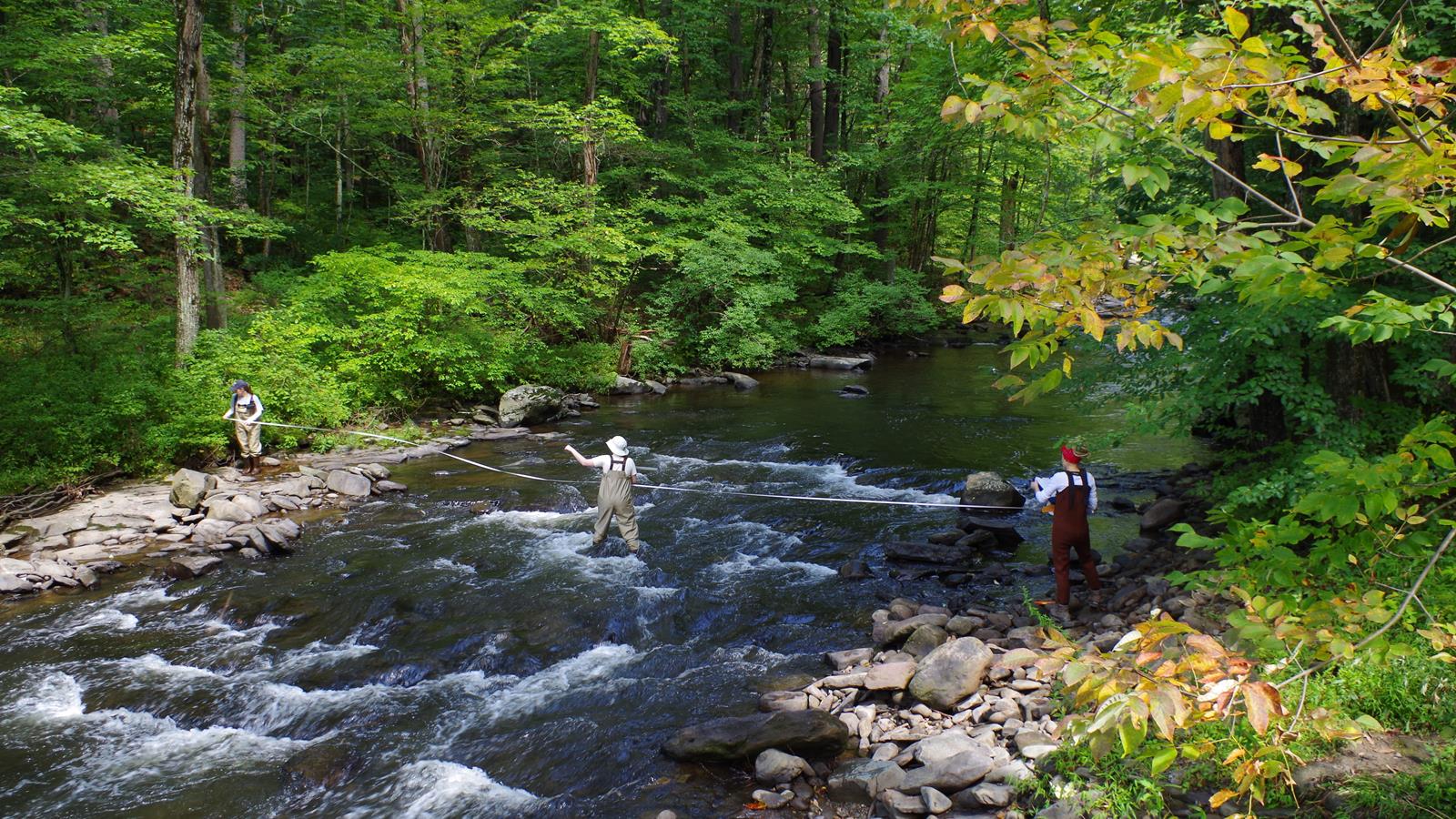 Three scientists measuring the width of a river from shore to shore.