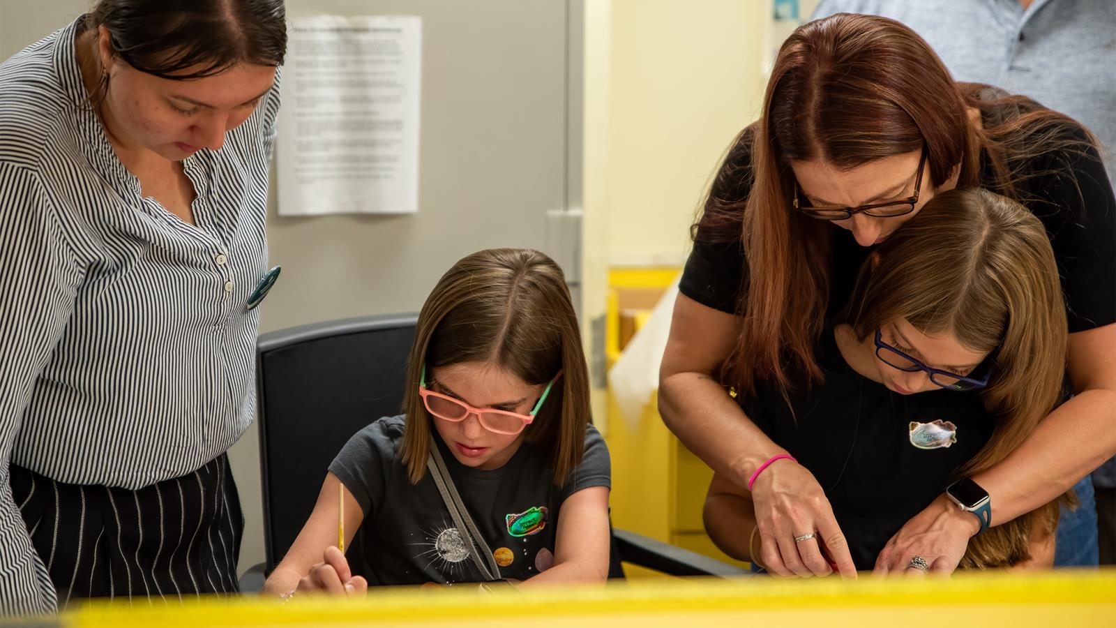 Two adults helping two children work on a craft.