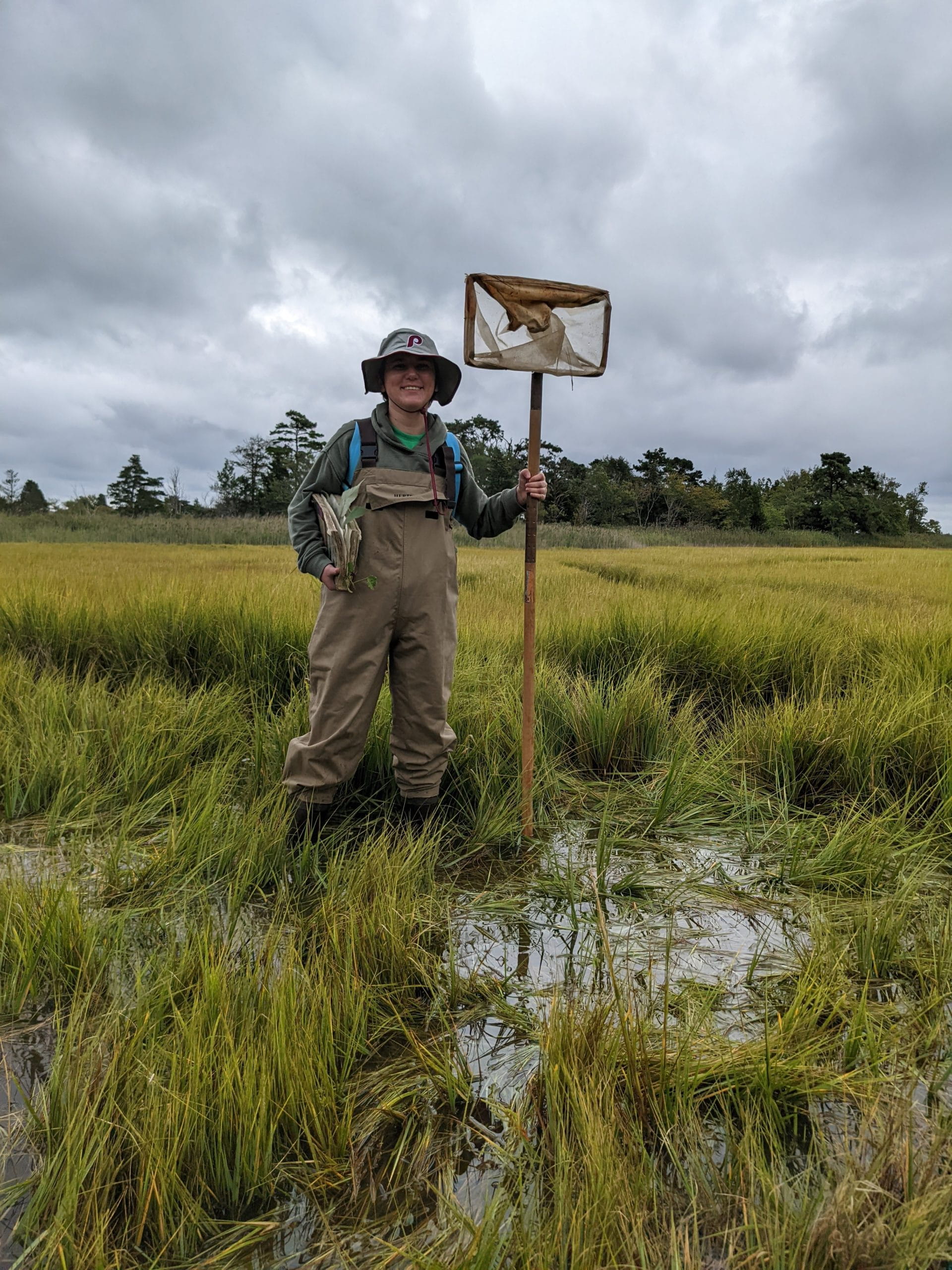 Tobias Tagliaferro standing in wetlands wearing waders and holding a net.