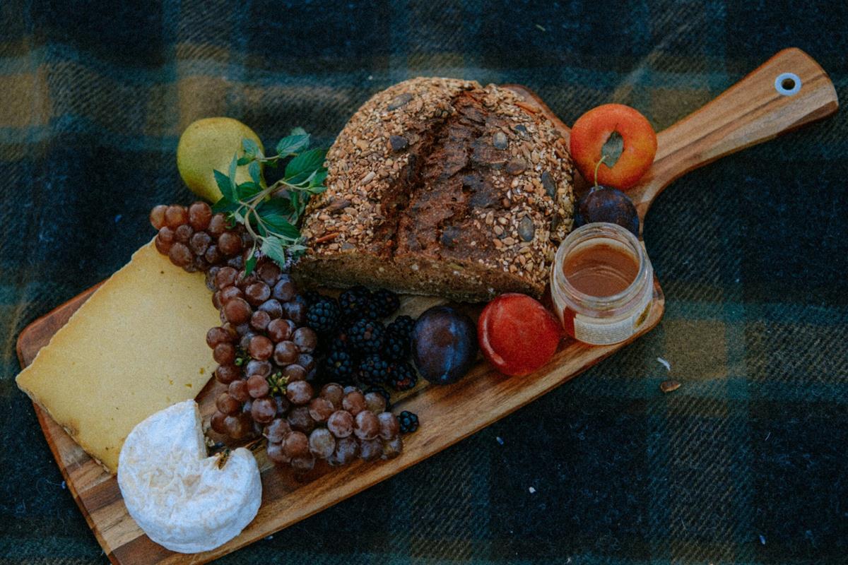 A charcuterie board with grapes, peppers, sauces, and cheese.