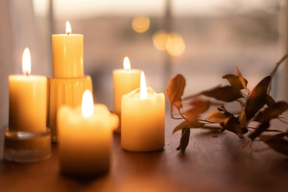 Several lit candles on a table next to decorative leaves.