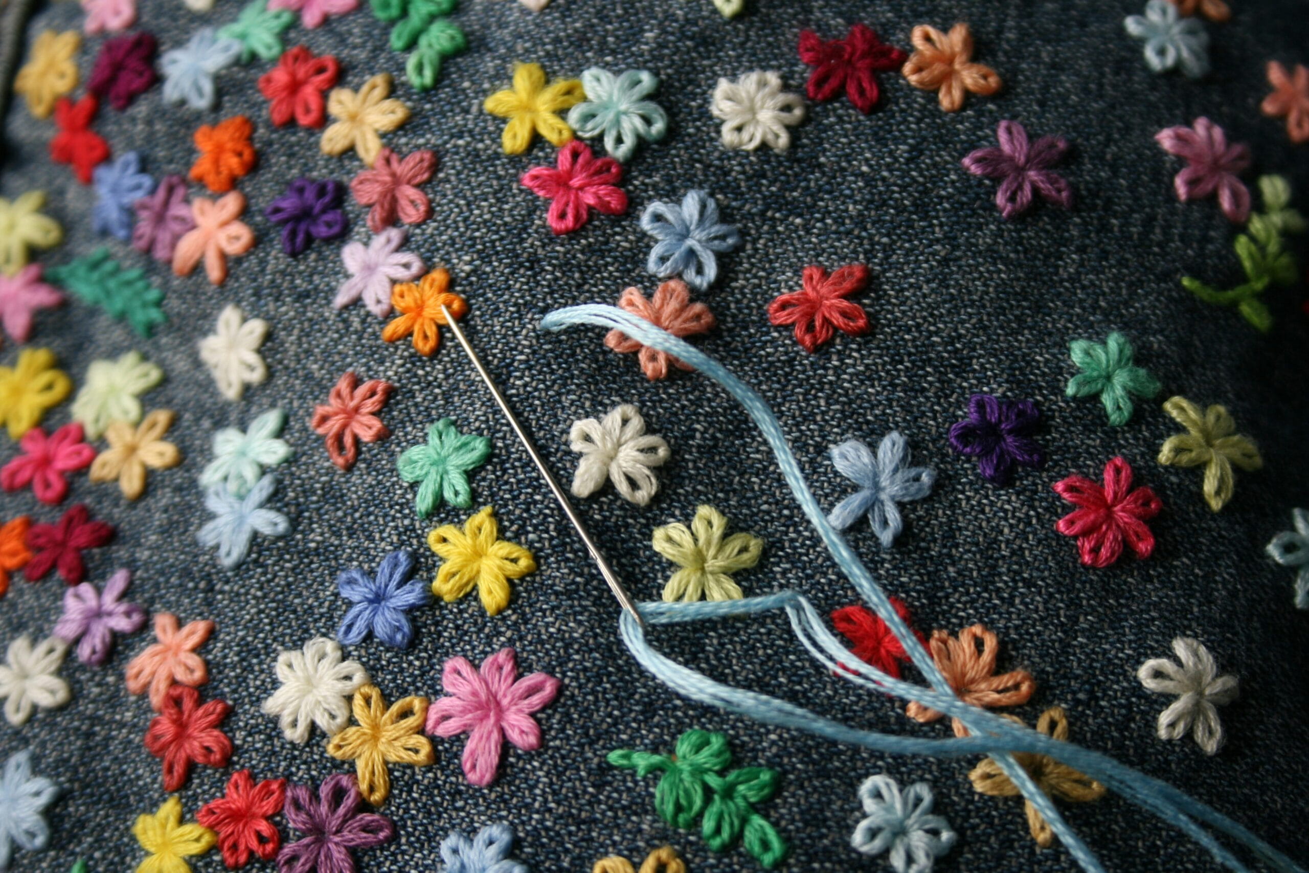 A needle and thread with multiple flowers hand sewed with a variety of colors.