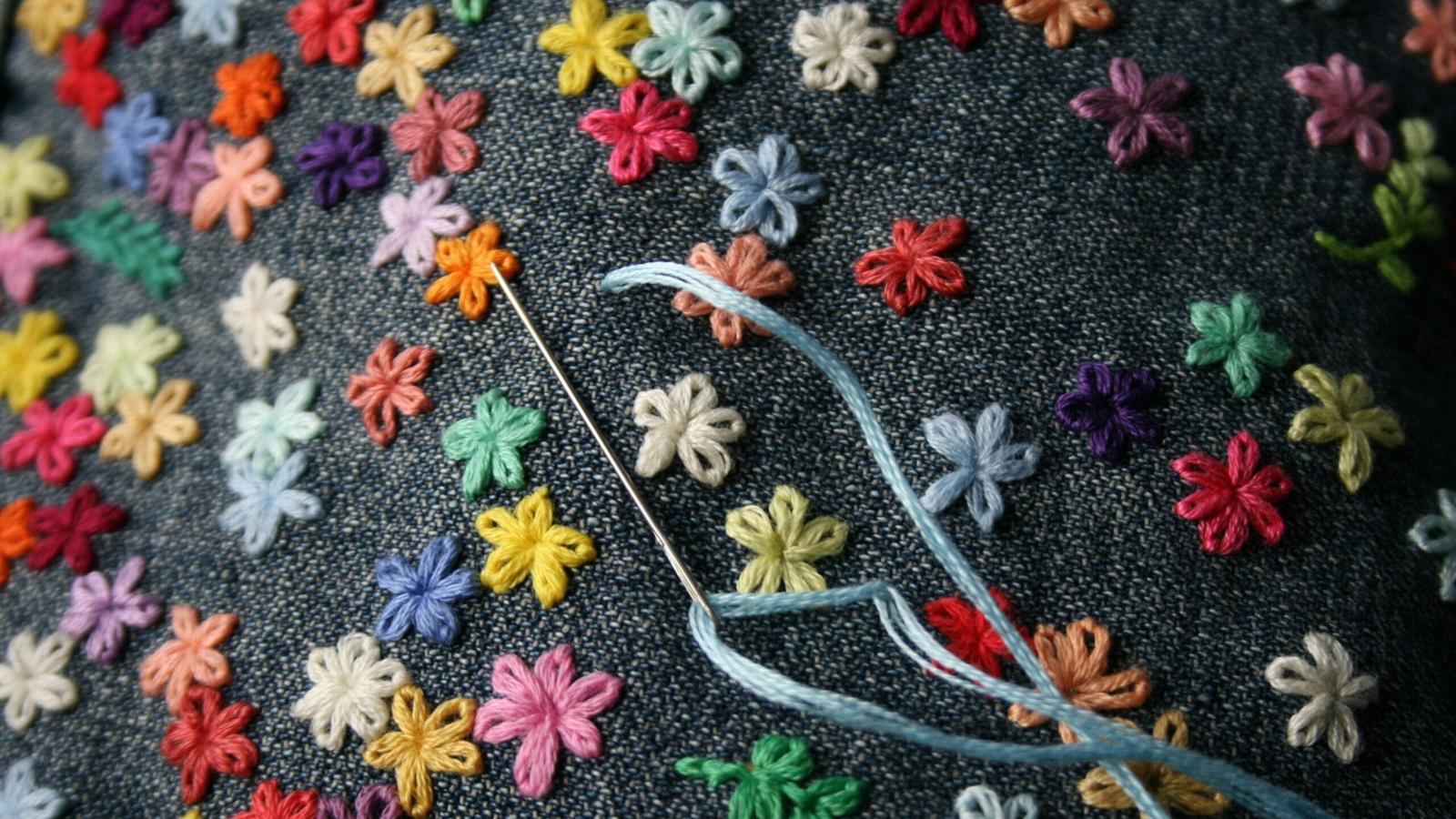 A needle and thread with multiple flowers hand sewed with a variety of colors.