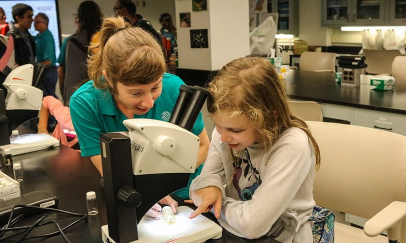 Female scientist and female child look under microscope