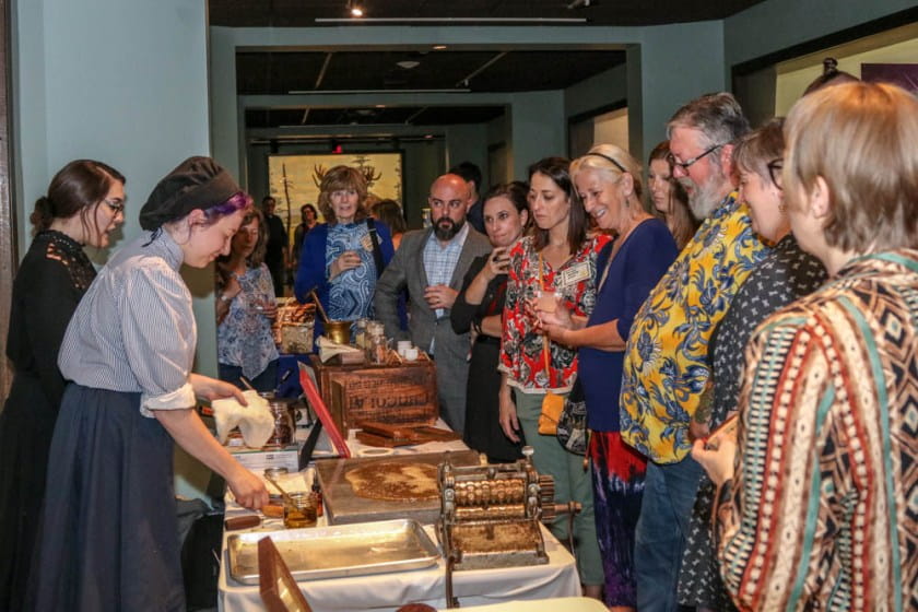 Women dressed in old timely clothing make candy in front of a group