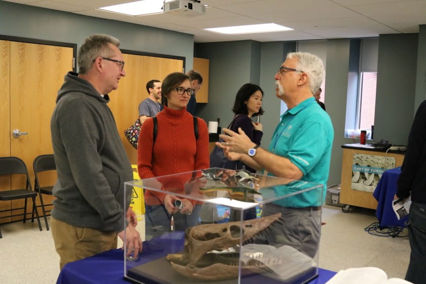 Two adults talk to Academy volunteer about marine reptile fossil in foreground