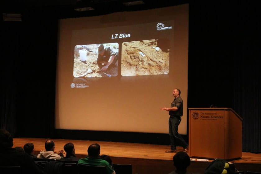 Man onstage with projected images onscreen of man digging in the dirt