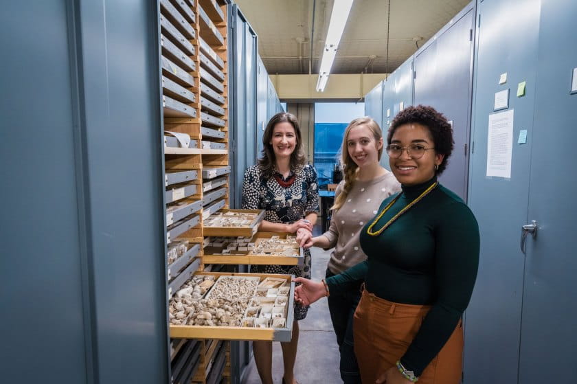 Three female scientists amidst Invert Paleo collection storage