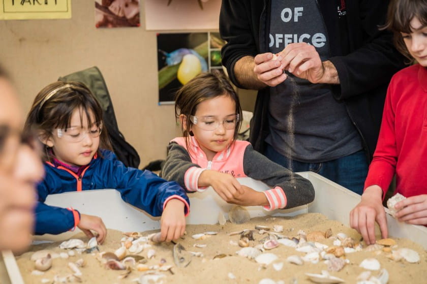 Two young girls dig for shells in a sandy pit