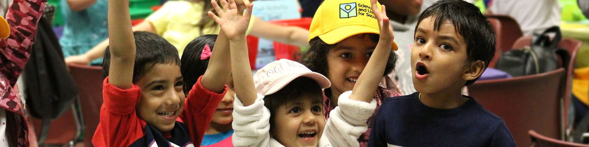 Children raise hands and smile during group activity