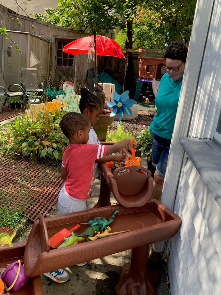 woman helps small children wash dinosaurs in colorful backyard