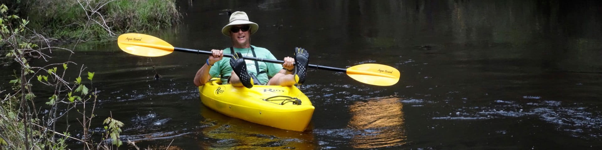 Man in sun hat paddles yellow kayak