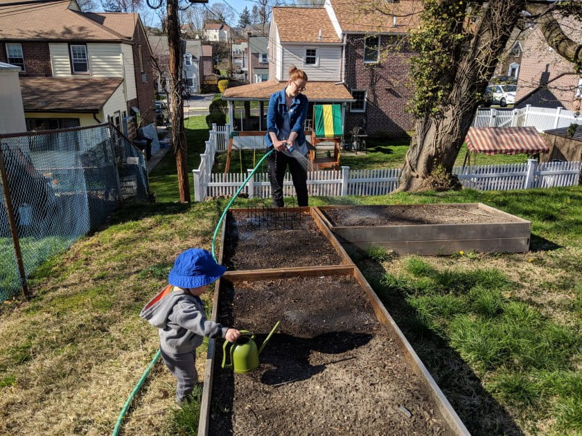 Woman and toddler water a garden bed