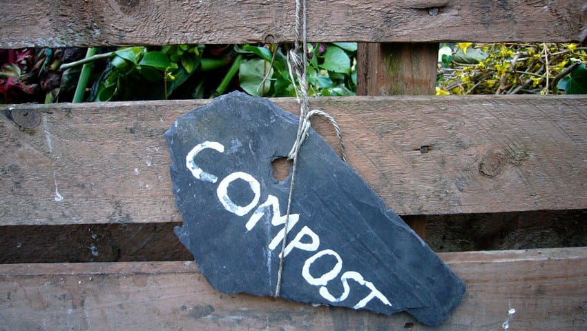 outside of wooden compost bin with black chalk sign with the word compost written on it in white