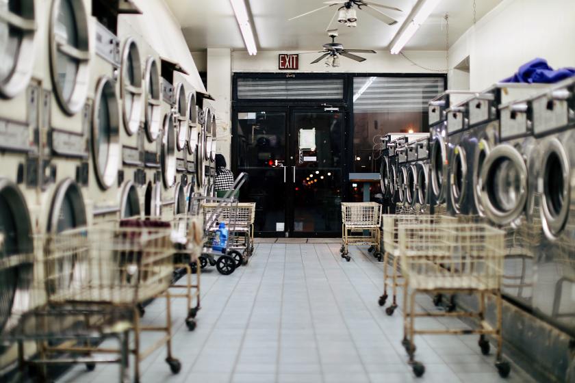 Empty laundromat with white tile floor, open laundry carts and silver machines, looking out toward the exit at nighttime