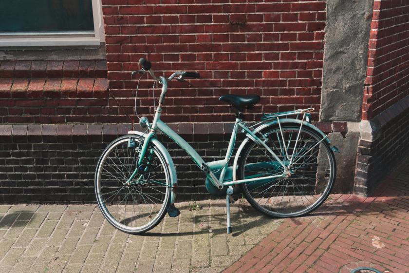 Robin's egg blue old fashioned bicycle with black seat and white kickstand leans against a brick building