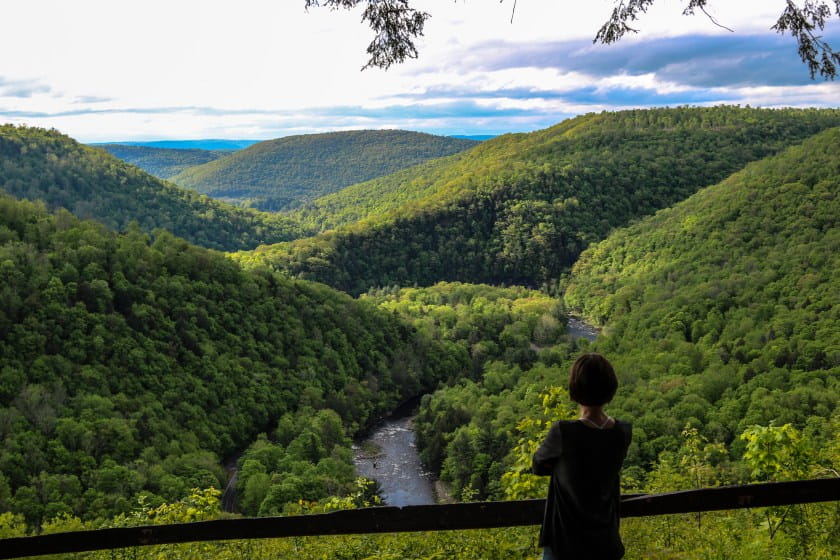 woman looking out over vista of green hills with river below