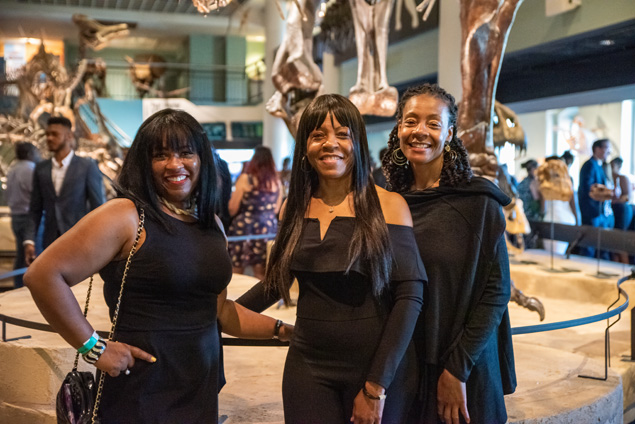 Three black women posing in front of the t-rex in dinosaur hall.