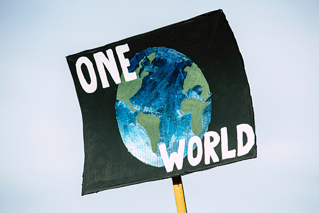 protest sign showing one world text over earth photo Photo by Markus Spiske on Unsplash