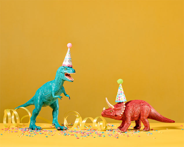 A blue t-rex dinosaur and a red triceratops wearing party hats on a yellow background.