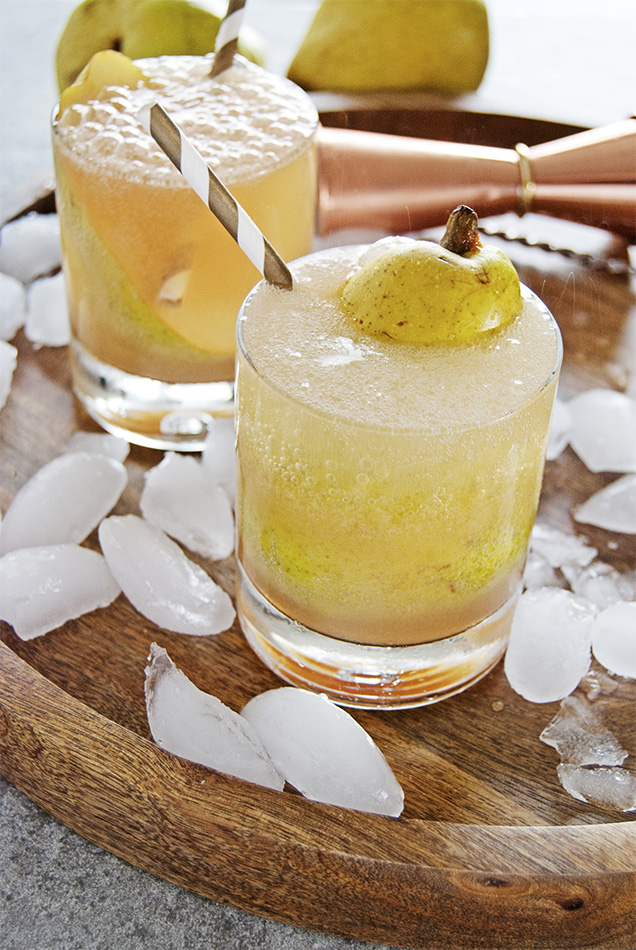 yellow drink in glass with pear on top surrounded by ice cubes