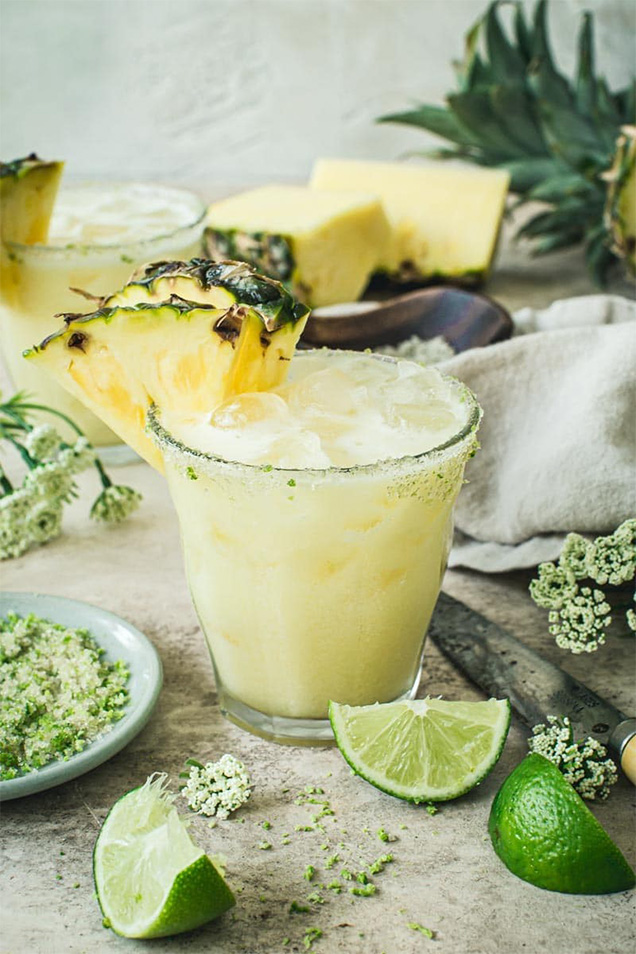 yellow fizzy drink in glass with pineapple and lime slices next to glass