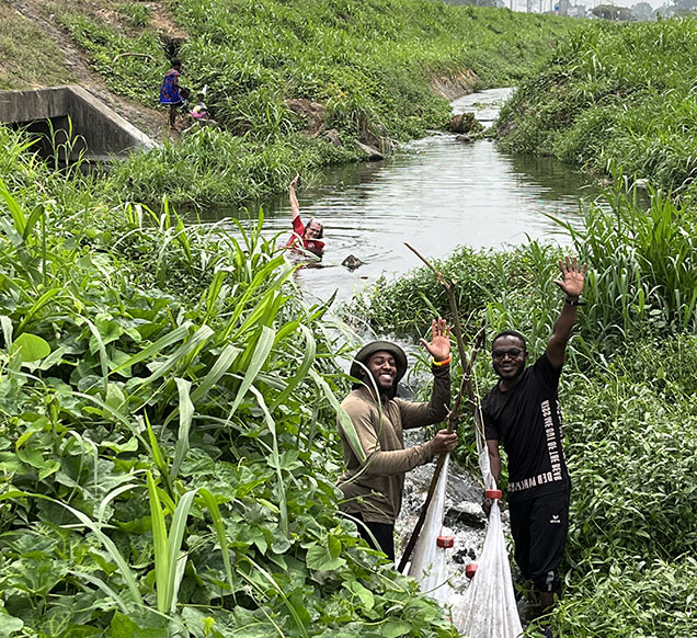 scientists with fishing net in small river with green vegetation