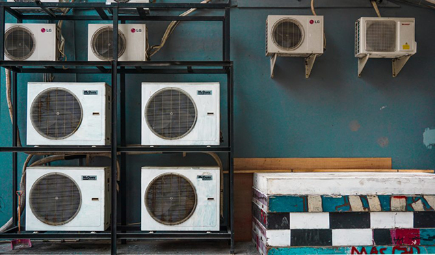 Eight air conditioners along a teal wall.