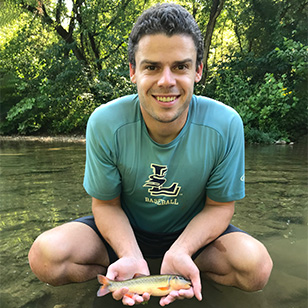 A scientist in a green shirt holding a fish kneeling in a river.