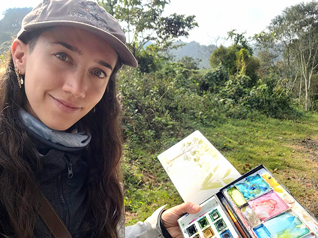 An image of artist Annamaria Drago in nature showing off their watercolor palette